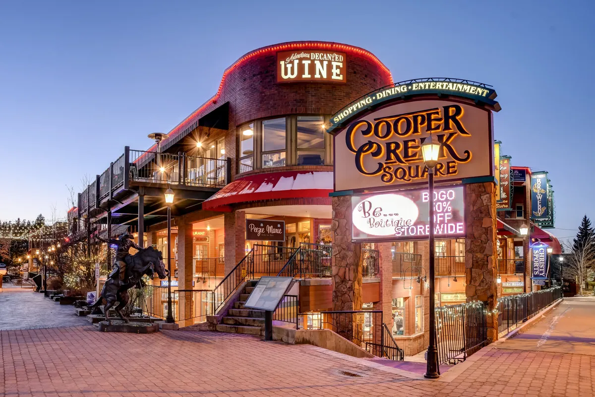 This lively exterior shot highlights the Cooper Creek Square sign, a wine shop entrance, and a staircase leading up into the energetic core of the local entertainment district. It captures a sense of activity, shopping, dining, and evening events, reflecting the vibrancy of nearby attractions.