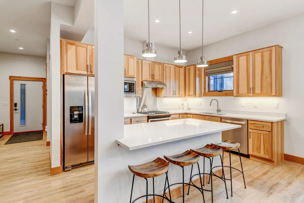 The image focuses on a gourmet kitchen complete with a granite island, wooden cabinets, stainless steel appliances, and bar stools. The setup is perfect for both cooking and entertaining, with ample counter space and contemporary finishes.