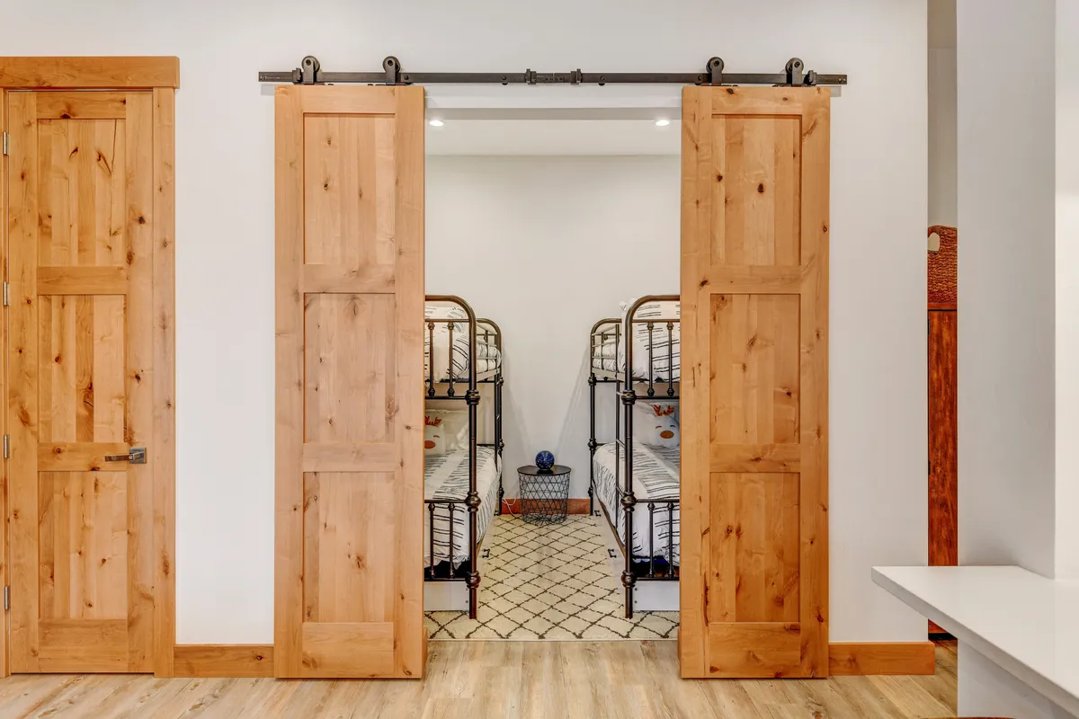 A playful and functional bunk room with two twin-over-twin bunk beds framed by sliding barn doors and accent decor. The space is designed for group or family stays, offering both fun and practicality for kids and larger groups.