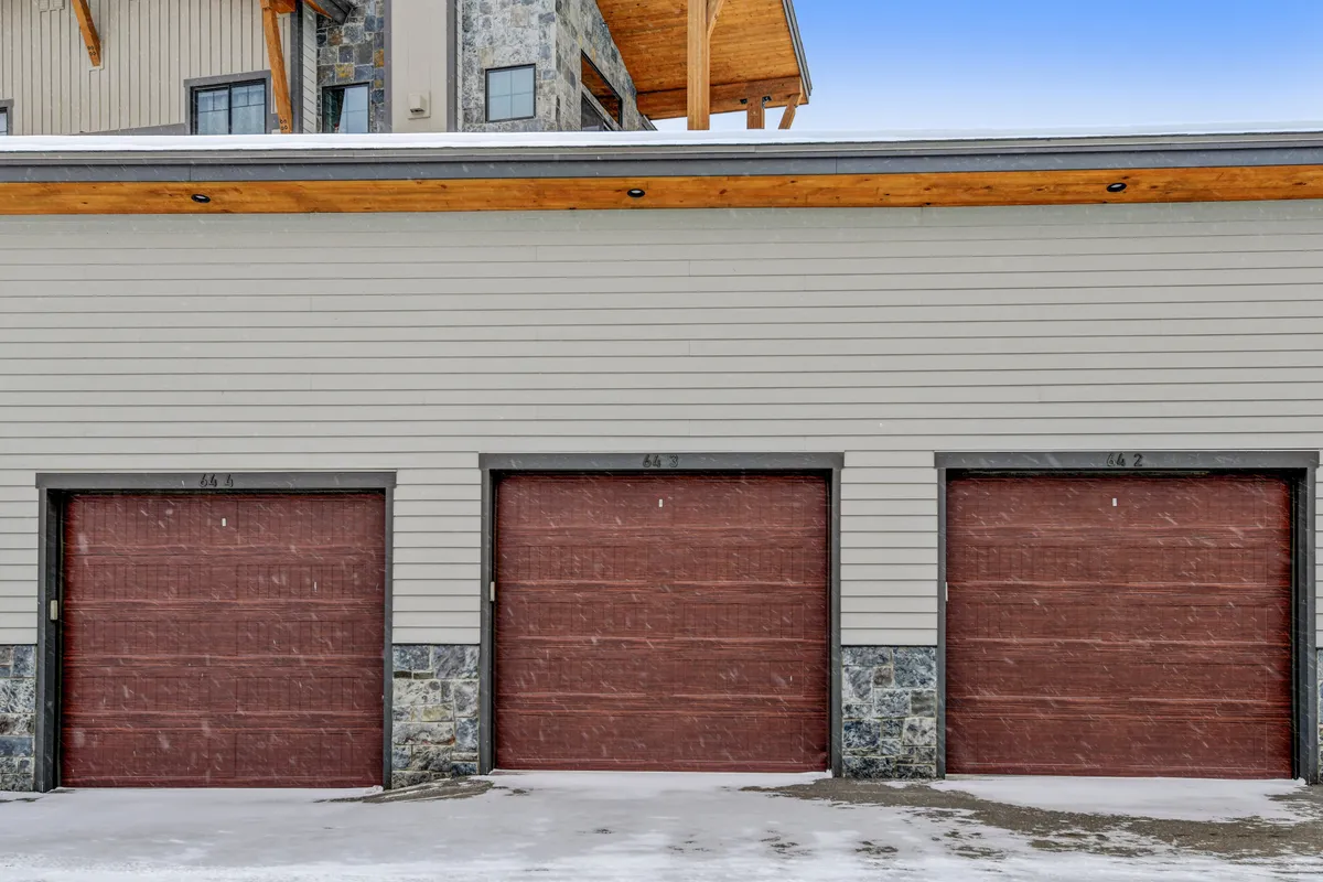 This exterior shot displays a home with three garage doors, a stone facade, and wooden overhang. The winter setting suggests secure garage parking, convenient access after snowy adventures, and a welcoming return from guest excursions.