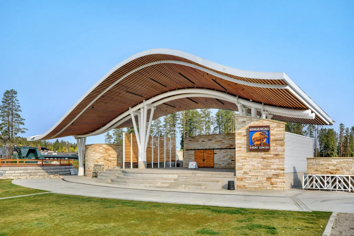 An outdoor amphitheater with a curved roof, stone walls, and a dedicated stage area, set up for a community concert or event. The open-air setting hints at live performances and gatherings, evoking the neighborhood’s festive, family-oriented spirit.