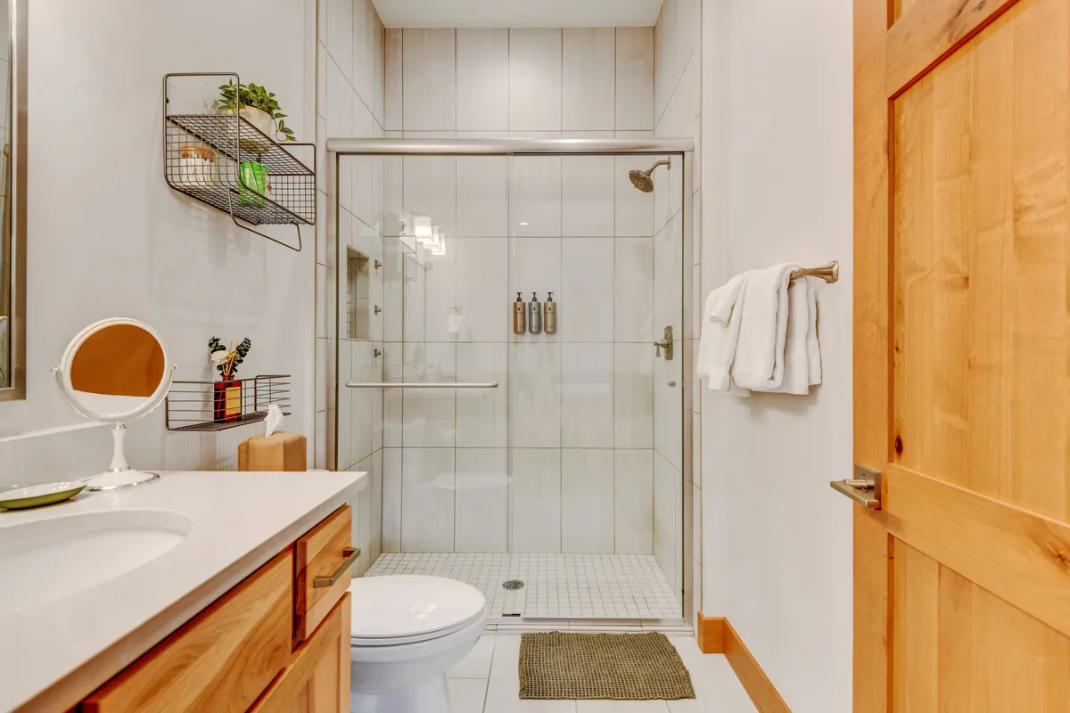 A bright, modern bathroom with a spacious glass-enclosed shower, a wooden vanity topped with a large mirror, and soft towels ready for use, evoking spa-like relaxation.