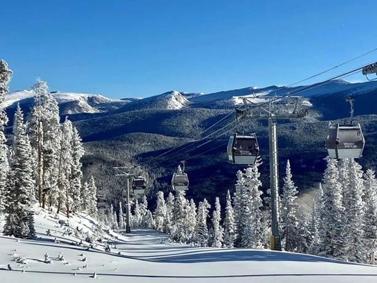 This exterior image showcases a panoramic view of gondola lifts gliding above snow-covered trees with a majestic mountain range in the background. The scene is vibrant and dynamic, evoking the thrill of ski adventures and mountain exploration, while also hinting at year-round scenic rides and hiking.