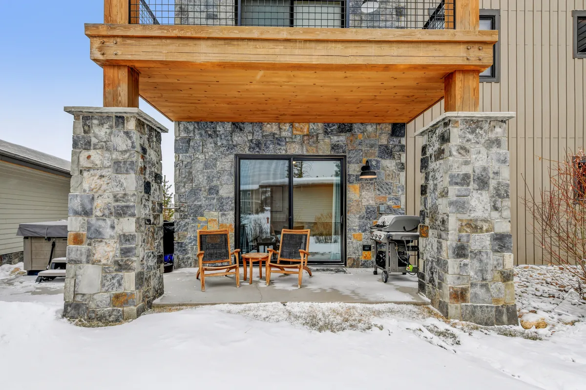 An outdoor deck with sturdy stone columns, wooden decking, comfortable outdoor seating, and a barbecue grill. The space is ideal for hosting sunset dinners, winter gatherings, or simply relaxing and socializing in a cozy, communal outdoor environment.