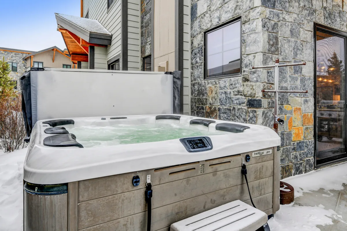 An inviting exterior image of a private hot tub nestled against a stone wall, surrounded by snow. The steamy, bubbling water contrasts with the winter scenery, suggesting relaxation and luxury after a day of mountain adventures.